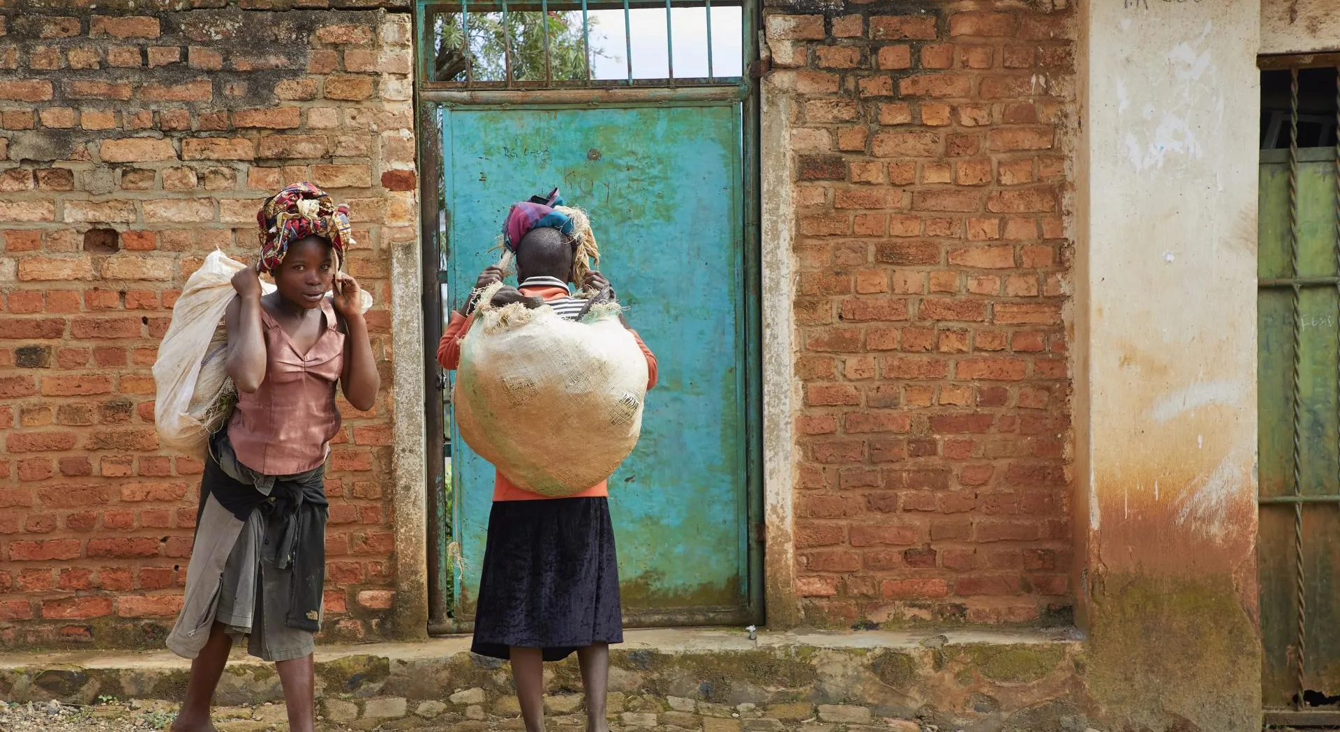 Kongo: Zwei Mädchen mit Säcken voll Nahrung vor ihrer Haustüre