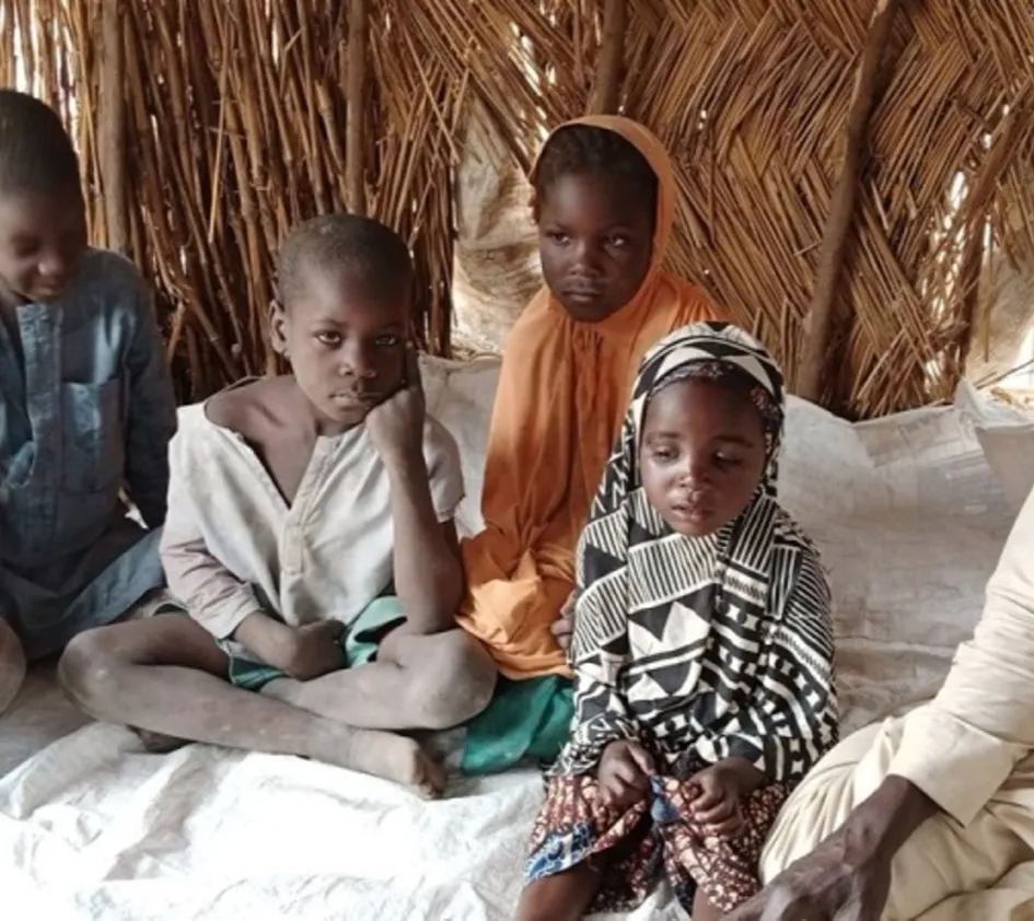 Auf der Flucht: Familie mit Kindern sitzt auf dem Boden eines Strohzelts