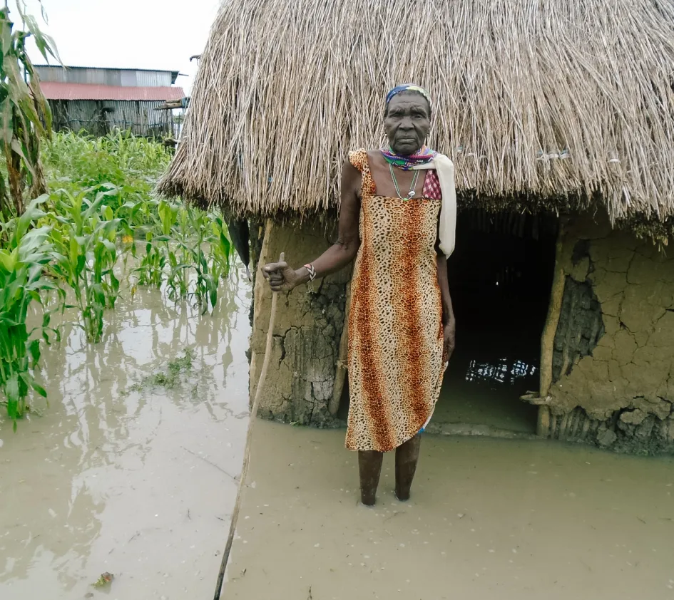 Kriterien: Ältere Dame im Südsudan steht vor ihrem Haus, das bis zum Eingang unter Wasser steht