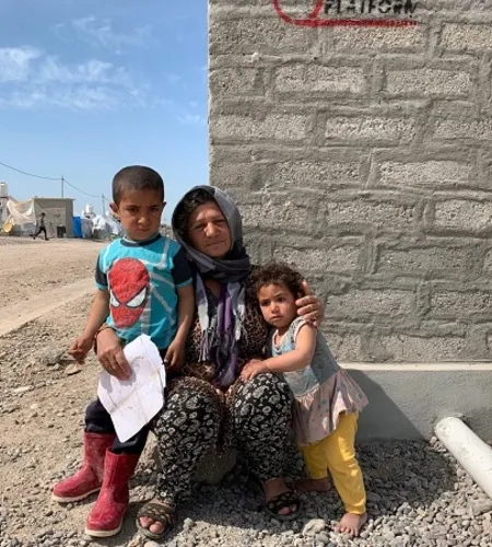Frau sitzt mit ihren Kindern vor einem Flüchtlingslager im Irak