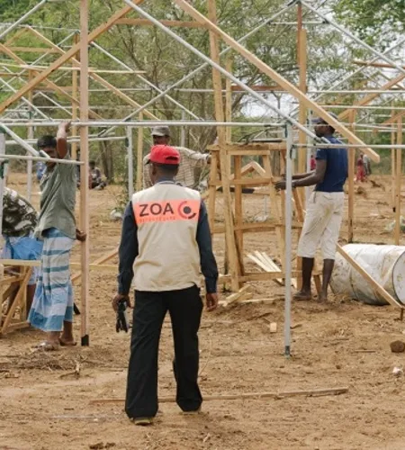 Mitarbeiter von ZOA steht vor einem Gerüst zum Hausbau