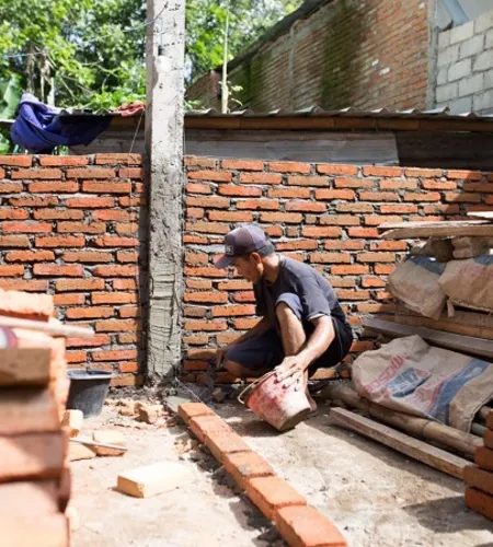 Mann schichtet Ziegel mit Zement zu einer Hauswand auf