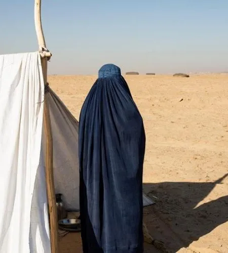 Afghanische Frau steht neben ihrem Zelt