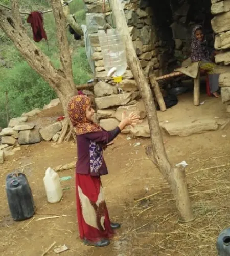 Mädchen wäscht Hände an einem am Baum aufgehängten Wasserkanister