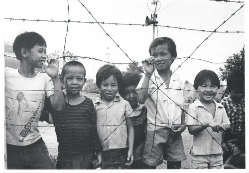 Schwarz-Weiß-Bild zeigt fünf Kinder aus Vietnam an einem Maschendrahtzaun