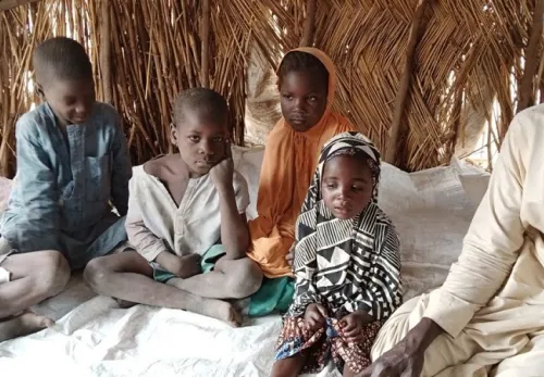 Auf der Flucht: Familie mit Kindern sitzt auf dem Boden eines Strohzelts